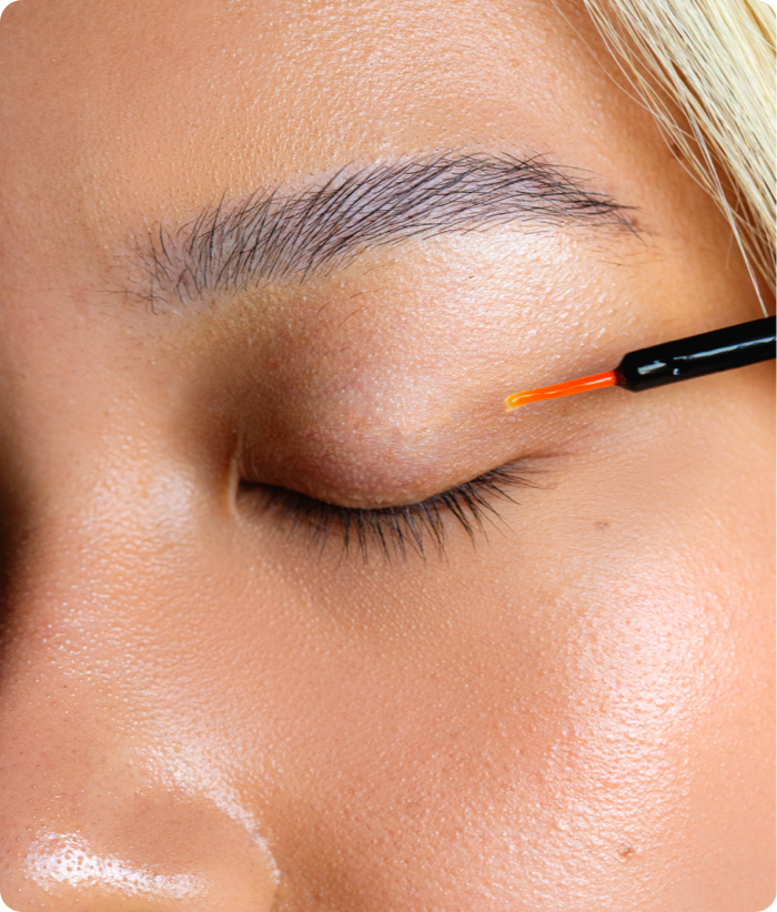 A close-up of a person's closed eye as a hand applies the Amplifeye® Advanced Lash & Brow Fortifier with a thin brush along the lash line.